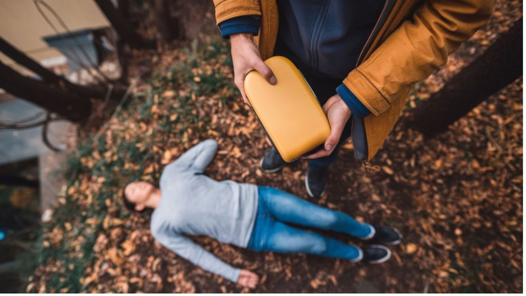 man holds defibrillator near unconscious person